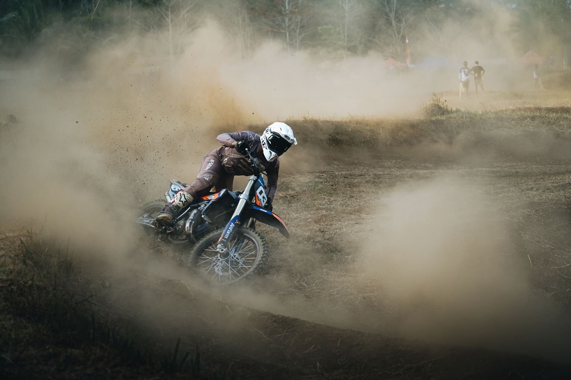 A rider kicks up dust on a dirt bike through a motocross track.