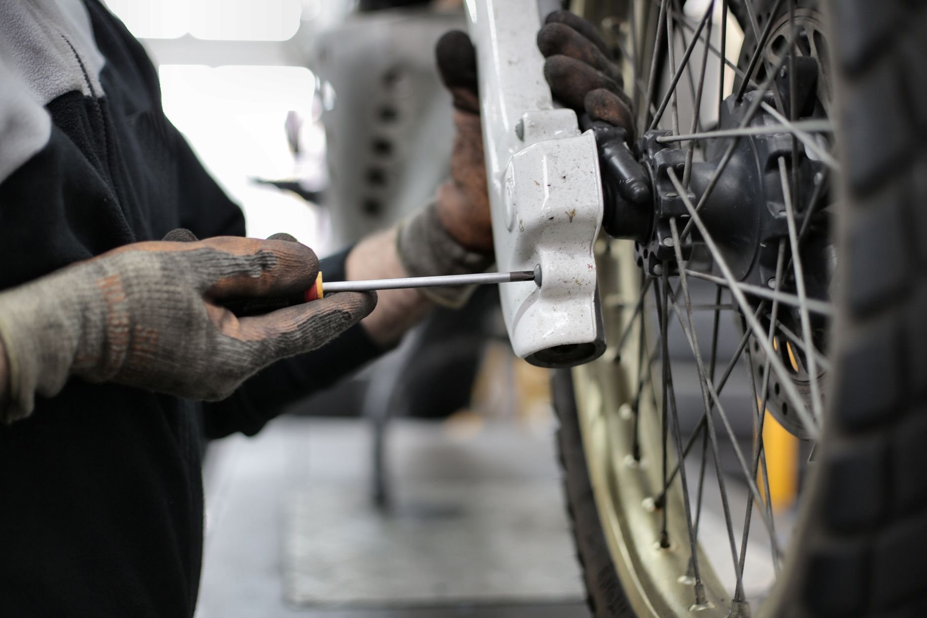 A mechanic's hands repair a motorcycle wheel with a screwdriver in a workshop.